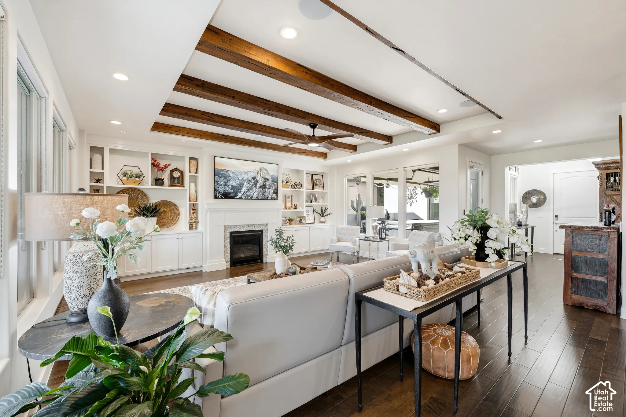 Living space featuring exposed ceiling beams, recessed lighting, a fireplace with a white mantel, built-in shelving, and wood-finish flooring