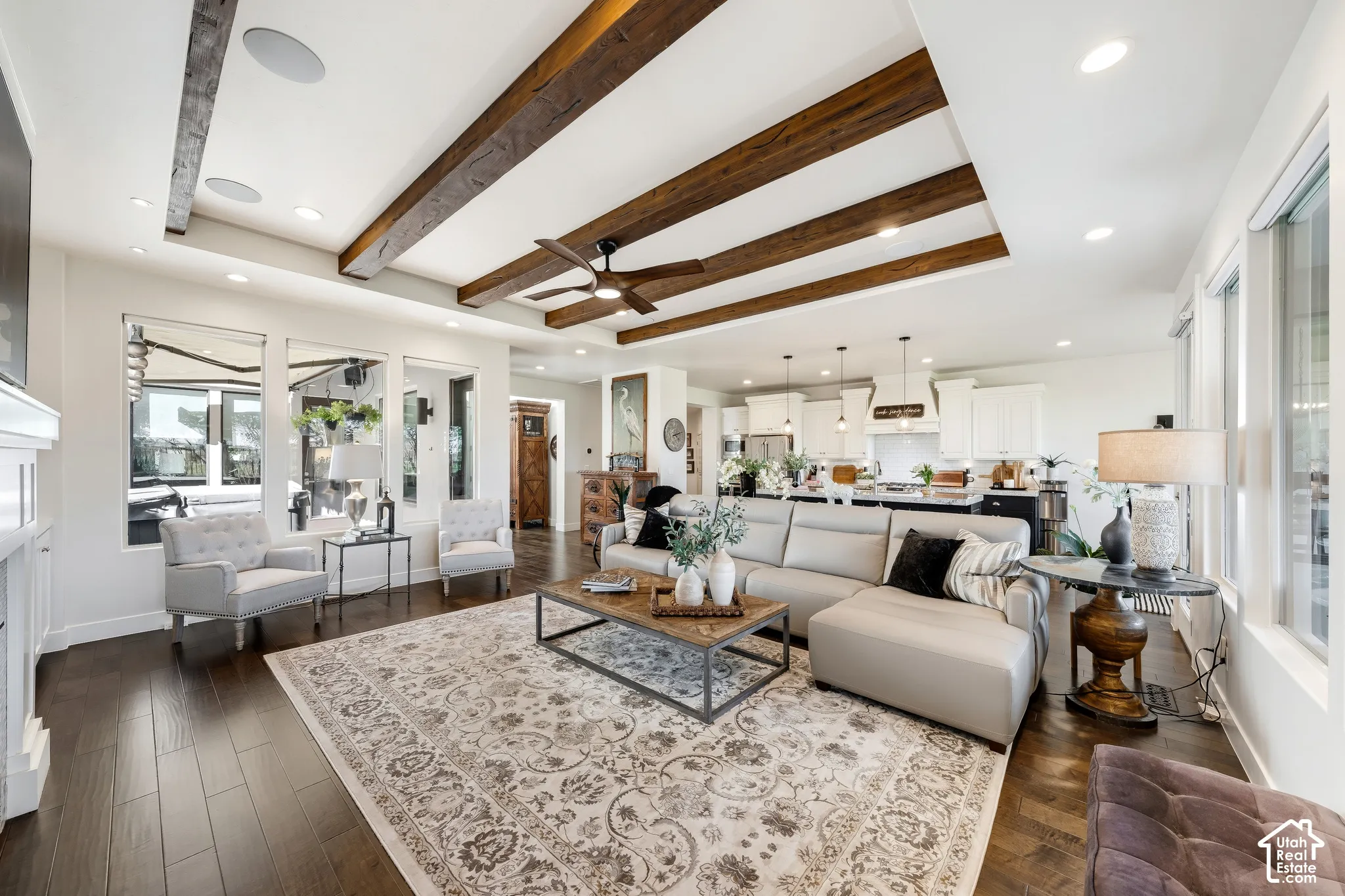 Open-concept living space featuring exposed wood-beam ceiling with recessed lighting, wide-plank wood-finish flooring throughout, and abundant natural light from multiple windows and glass doors