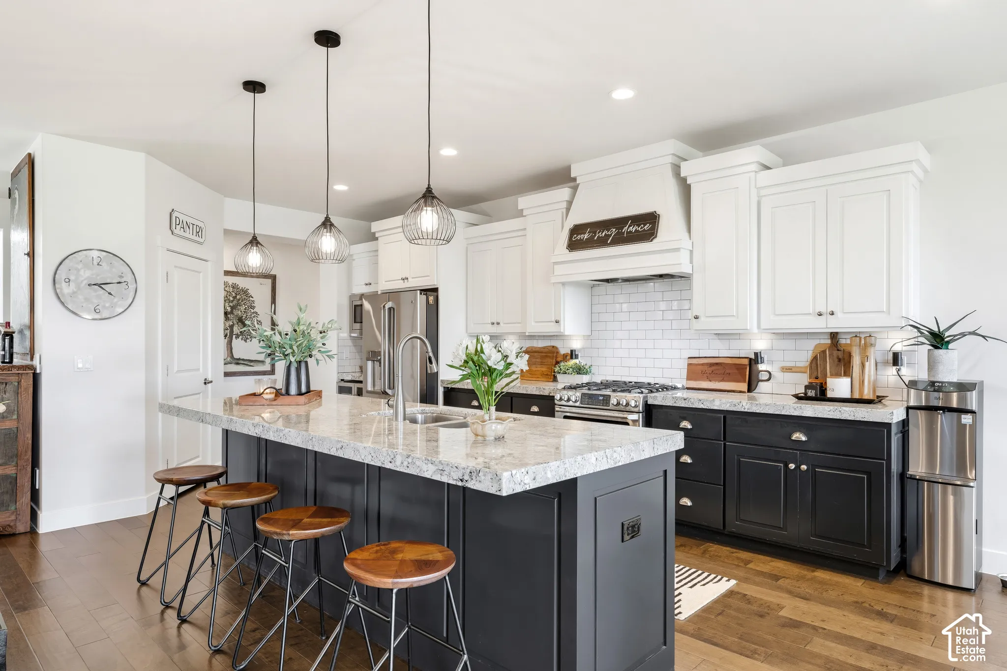 Chef's kitchen featuring white cabinetry with shaker-style doors, a contrasting dark-finished island with quartz countertop, stainless steel appliances including a gas range, subway tile backsplash, pendant lighting, and wood-finish flooring throughout th