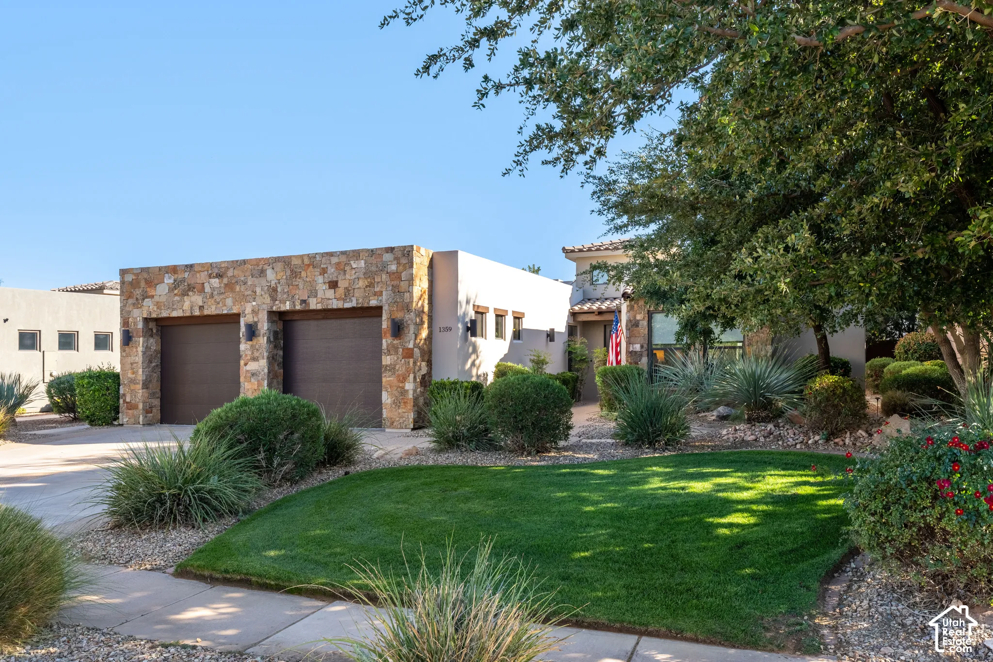 Two-car garage with stone veneer facade, mature landscaping, and a manicured lawn