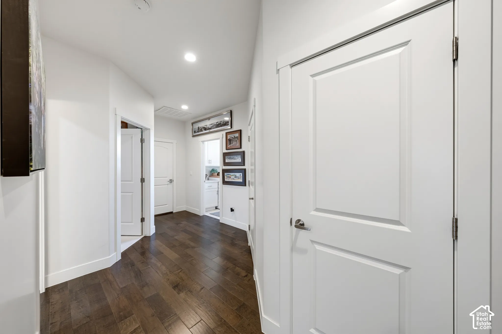 Hallway featuring dark wood-finish flooring, recessed lighting, and multiple white panel doors with polished hardware