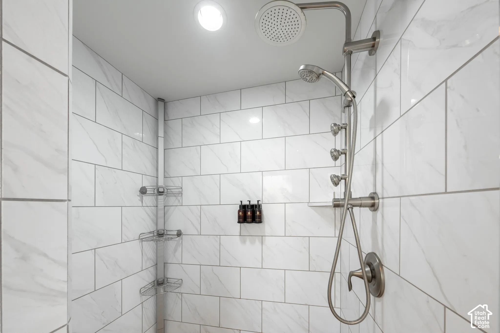 Shower enclosure featuring white subway tile, recessed lighting, a rainfall showerhead, and a multi-function shower system with a handheld sprayer