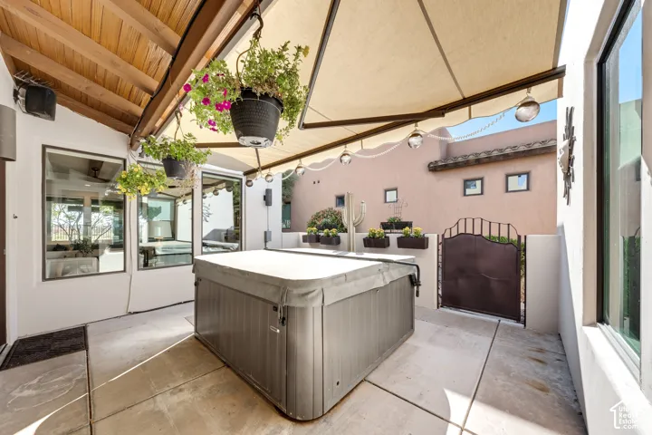 Covered patio with exposed wood beams, concrete flooring, built-in spa, and a wrought iron gate