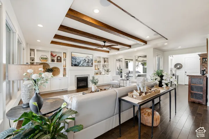 Living space featuring exposed ceiling beams, recessed lighting, a fireplace with a white mantel, built-in shelving, and wood-finish flooring