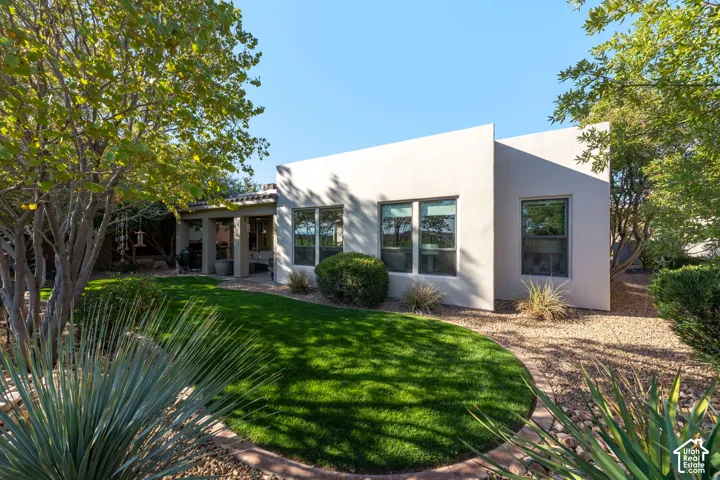 Stucco exterior with multiple windows, a covered patio area, and a manicured lawn