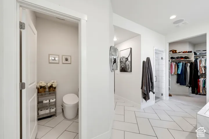 Primary bathroom and walk-in closet featuring tile flooring in herringbone pattern, recessed lighting, white subway tile shower surround with glass enclosure, floating vanity, and built-in shelving with hanging rod and organized storage systems