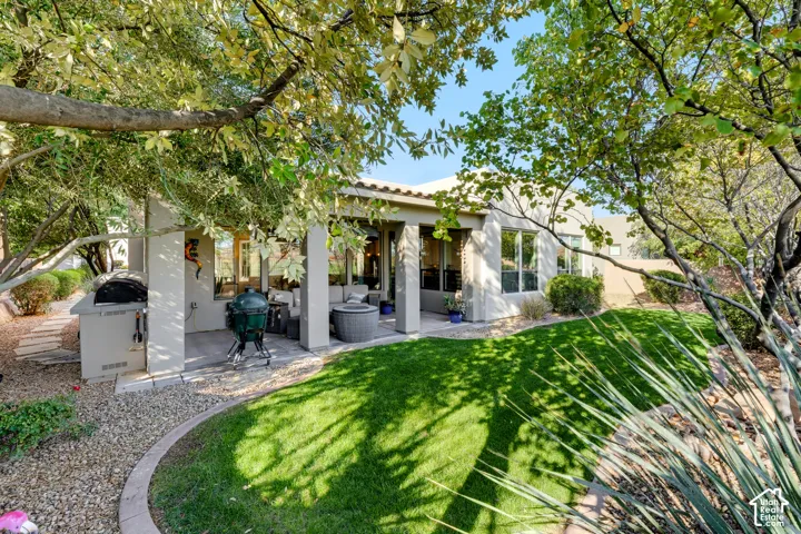 Expansive backyard featuring a manicured lawn, established shade trees, a built-in outdoor grill station, and a covered patio with recessed lighting