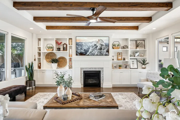 Vaulted ceiling with exposed wood beams, recessed lighting, built-in shelving, white mantel fireplace with tile surround, and wood-finish flooring