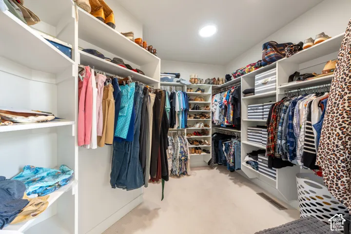 Walk-in closet featuring built-in white shelving, multiple hanging rods, recessed lighting, and carpeted flooring