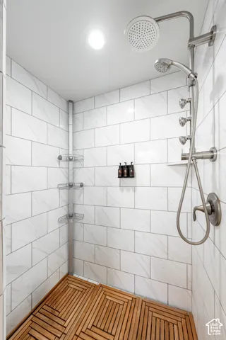 White subway tile walls with subtle veining, recessed ceiling lighting, and a multi-function shower system