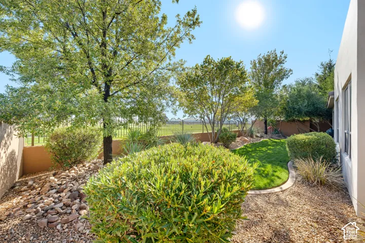 Mature trees, manicured lawn, gravel landscaping, stucco exterior, and a wrought iron fence