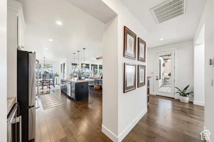 Open-concept kitchen and dining area showcasing wood-finish flooring throughout, recessed ceiling lighting, and a central island with dark cabinetry