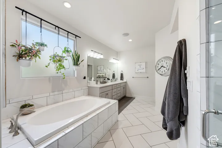 Recessed soaking tub with surrounding white tile, dual vanity with undermount sinks, and a glass-enclosed shower