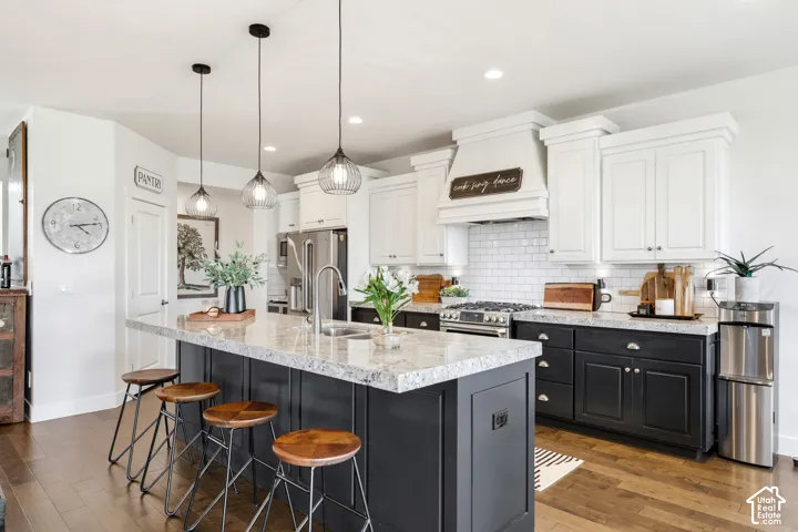 Chef's kitchen featuring white cabinetry with shaker-style doors, a contrasting dark-finished island with quartz countertop, stainless steel appliances including a gas range, subway tile backsplash, pendant lighting, and wood-finish flooring throughout th
