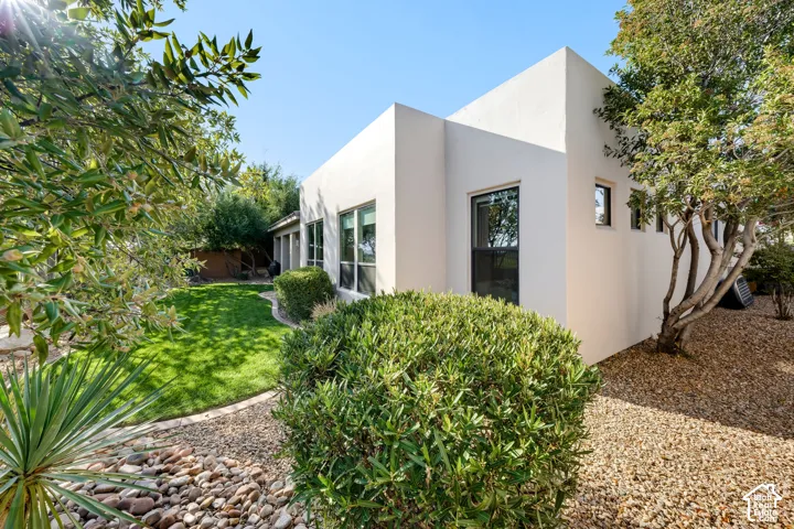 Contemporary stucco exterior with multiple windows, a manicured lawn, gravel landscaping, and mature trees