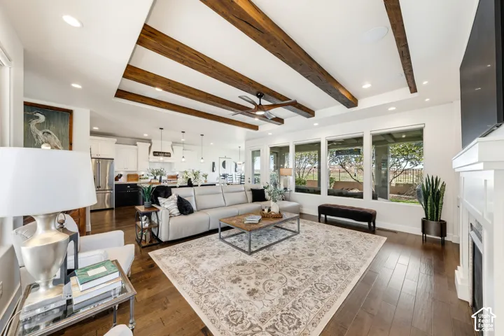 Open-concept living space with dark wood-finish flooring, a tray ceiling featuring exposed wood beams, and recessed lighting