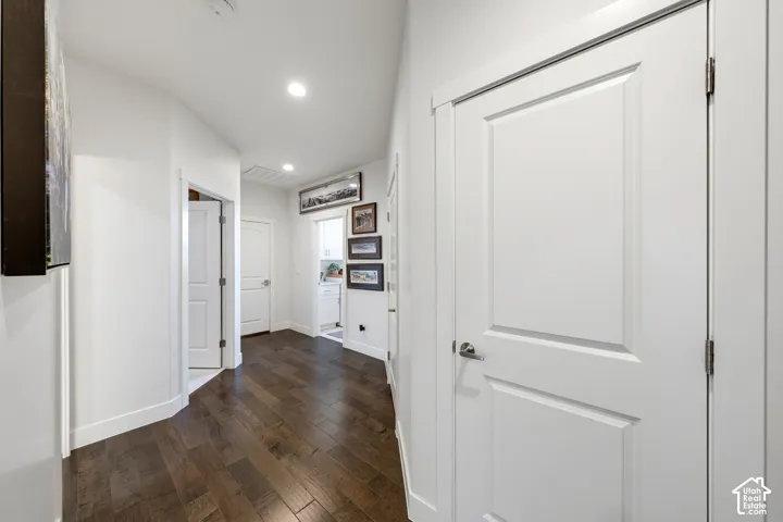 Hallway featuring dark wood-finish flooring, recessed lighting, and multiple white panel doors with polished hardware
