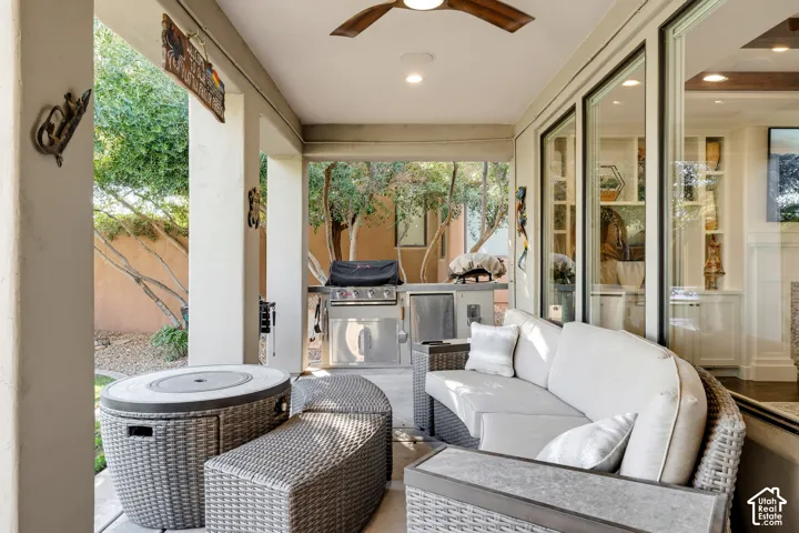 Covered patio with sliding glass doors opening to a landscaped outdoor space, featuring woven rattan seating with cushions, built-in outdoor grill, and ceiling fan