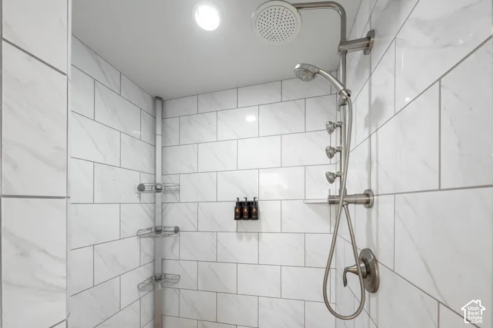 Shower enclosure featuring white subway tile, recessed lighting, a rainfall showerhead, and a multi-function shower system with a handheld sprayer