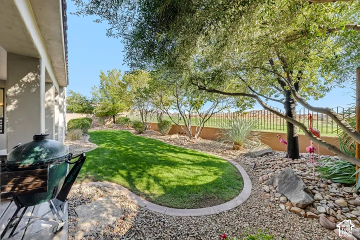 Expansive backyard oasis featuring a manicured lawn with curved hardscaping borders, mature shade trees, decorative rock landscaping, and metal fencing