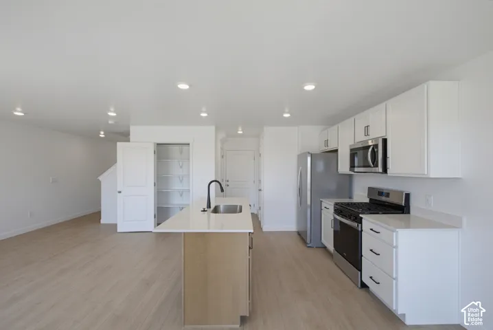 Kitchen featuring white cabinetry, stainless steel appliances, a center island with sink, and wood-finish flooring