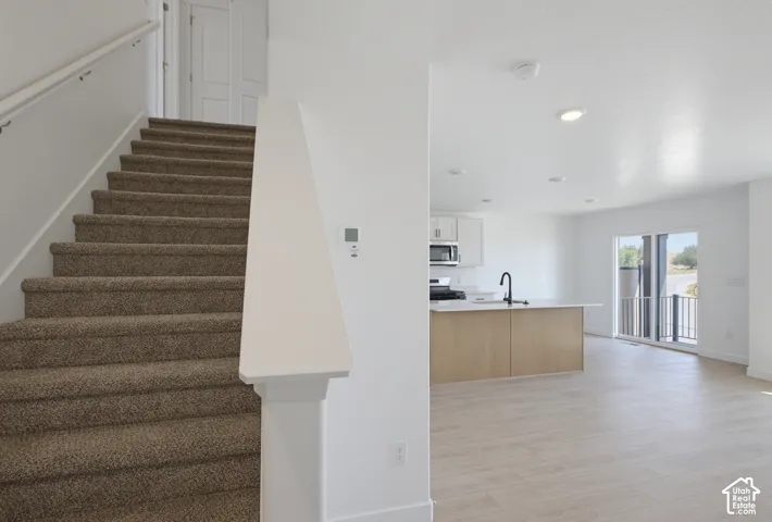 Open-concept living space featuring wood-finish flooring, recessed lighting, a modern kitchen island with seating, a sliding glass door, and a staircase with carpeted treads