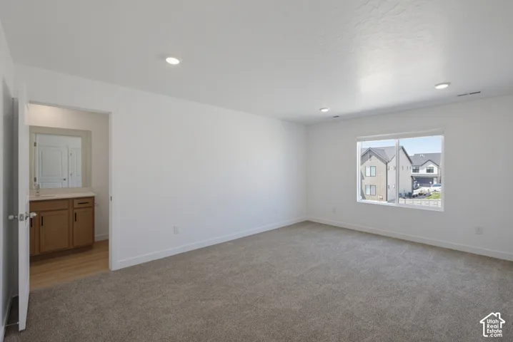Plush carpeting, recessed ceiling lighting, a large window, and an attached vanity with wood cabinetry and a countertop