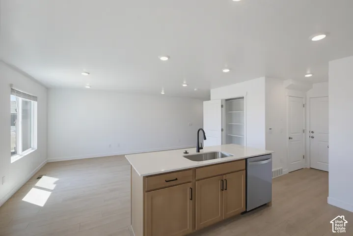 Kitchen island with integrated sink, stainless steel dishwasher, light wood-finish cabinetry, and recessed lighting