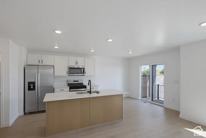 Kitchen featuring white shaker cabinetry, stainless steel appliances, a center island with a light-toned countertop, and wood-finish flooring