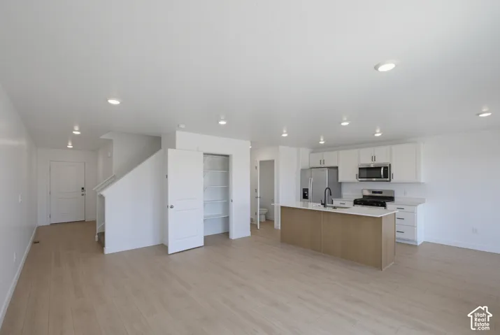 Wood-finish flooring, recessed lighting, white shaker cabinetry, stainless steel appliances, and a central island with a sink
