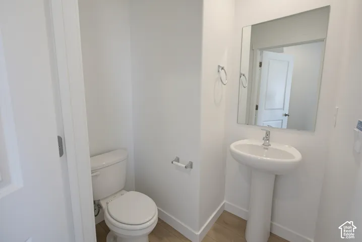 White pedestal sink with chrome faucet, a rectangular wall-mounted mirror, and wood-finish flooring