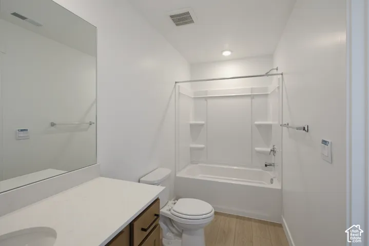White vanity with a light-toned countertop, wood-finish flooring, full-width mirror, and a white tub with an integrated shower