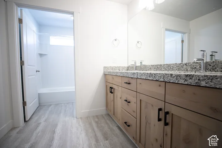 Primary bath with dual sinks, stained wood cabinets and granite slab countertops adjacent to large walk-in closet as part of primary suite.