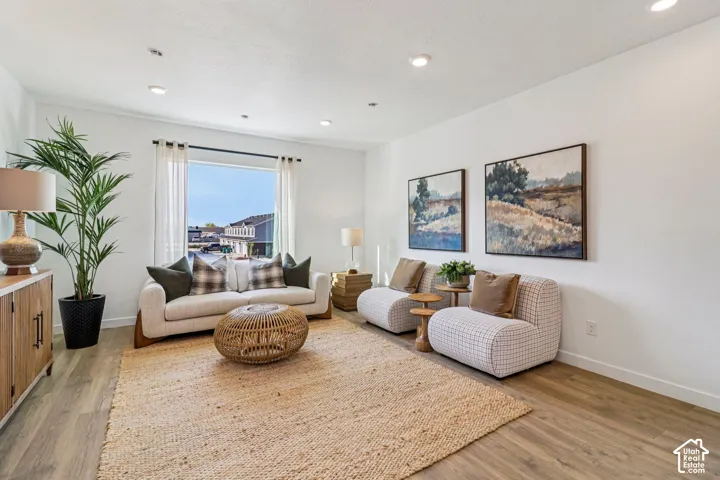 Recessed ceiling lighting illuminates a bright living space featuring wood-finish flooring and a large window
