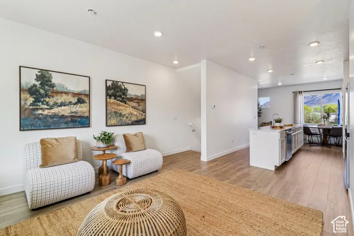 Recessed lighting throughout, wood-finish flooring, white kitchen island with seating, a window with a mountain backdrop, and light-toned walls