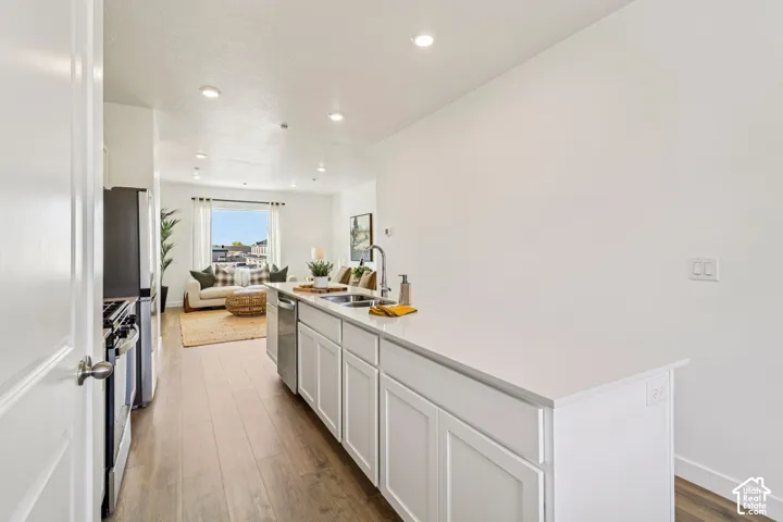 Open-concept living area with wood-finish flooring, recessed lighting, and a kitchen island featuring a stainless steel sink