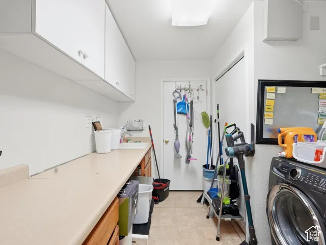 Laundry space featuring a single basin sink, white upper cabinetry, and a light-toned countertop