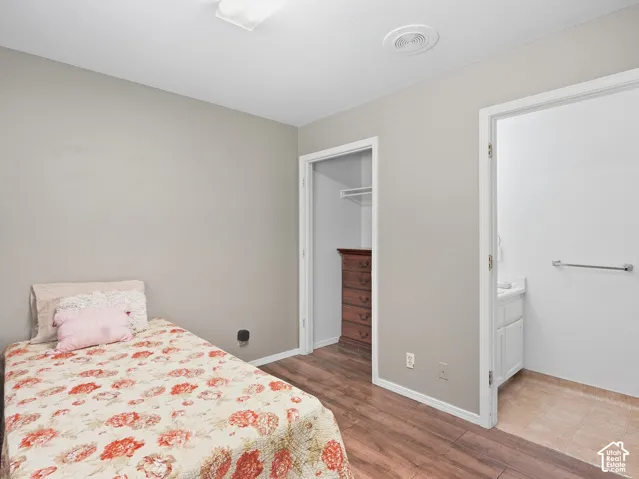 Wood-finish flooring, recessed ceiling light, closet with shelving, white vanity with integrated sink, and white wall paint