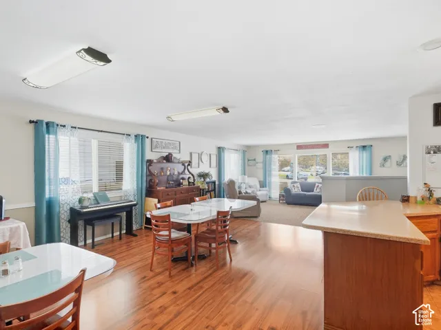 Wood-finish flooring, recessed lighting, built-in breakfast bar with a light-toned countertop, and multiple windows with blinds