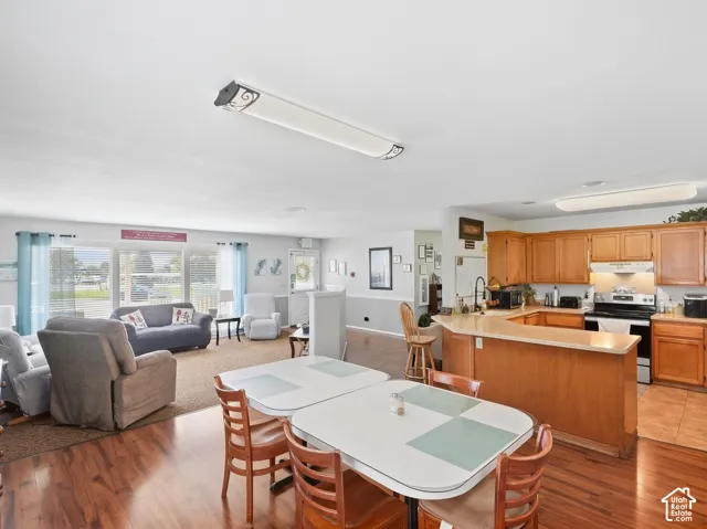 Wood-finish flooring throughout, full kitchen with wood cabinetry and built-in appliances, large windows with blinds, and recessed lighting fixtures