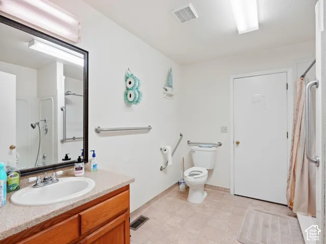 Bathroom featuring a wood-finish vanity with an integrated sink, a large wall mirror, and a shower with grab bars