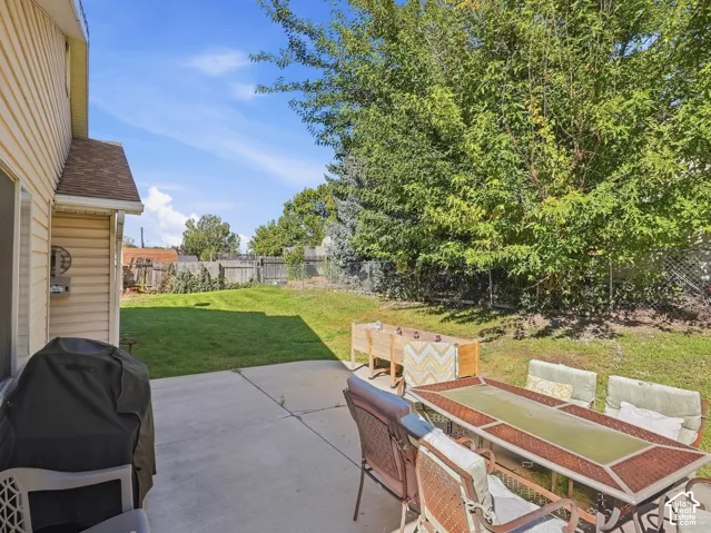 Expansive concrete patio with direct access to a large grass yard, surrounded by mature trees and a privacy fence