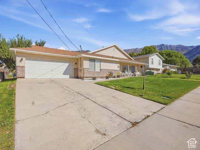 Attached two-car garage, concrete driveway, covered porch, and front yard with mature landscaping