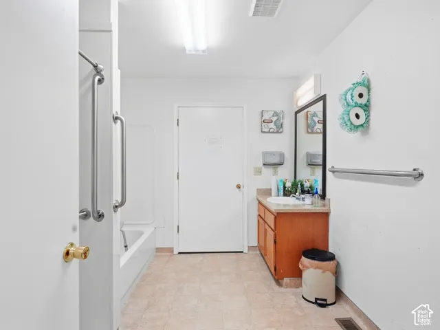 White bathroom with a tub/shower combination, grab bars, a single vanity with wood-finish cabinetry, and a rectangular mirror