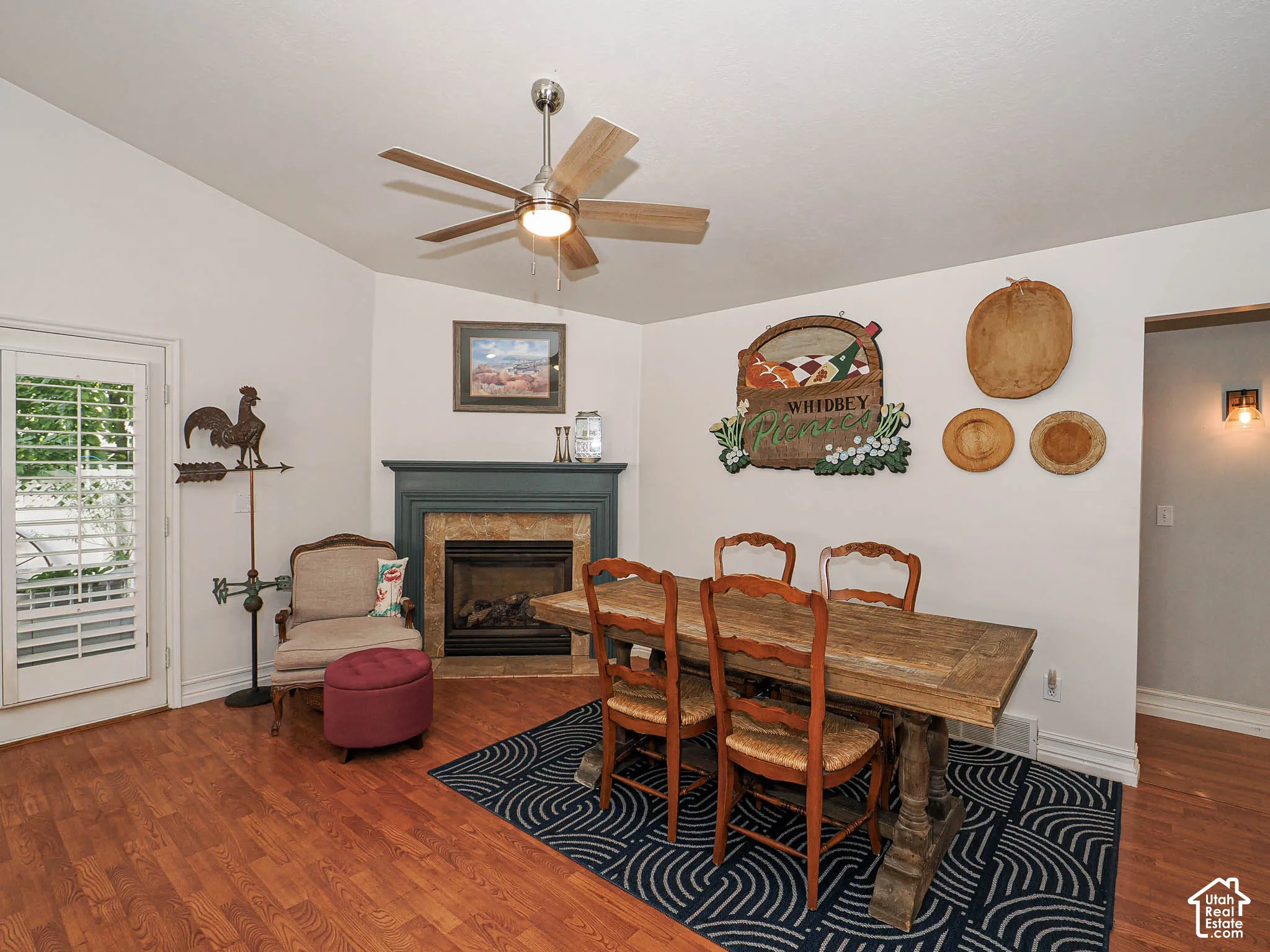 Vaulted ceiling with a ceiling fan, fireplace with a mantel and tile surround, French door with louvered blinds, and wood-finish flooring