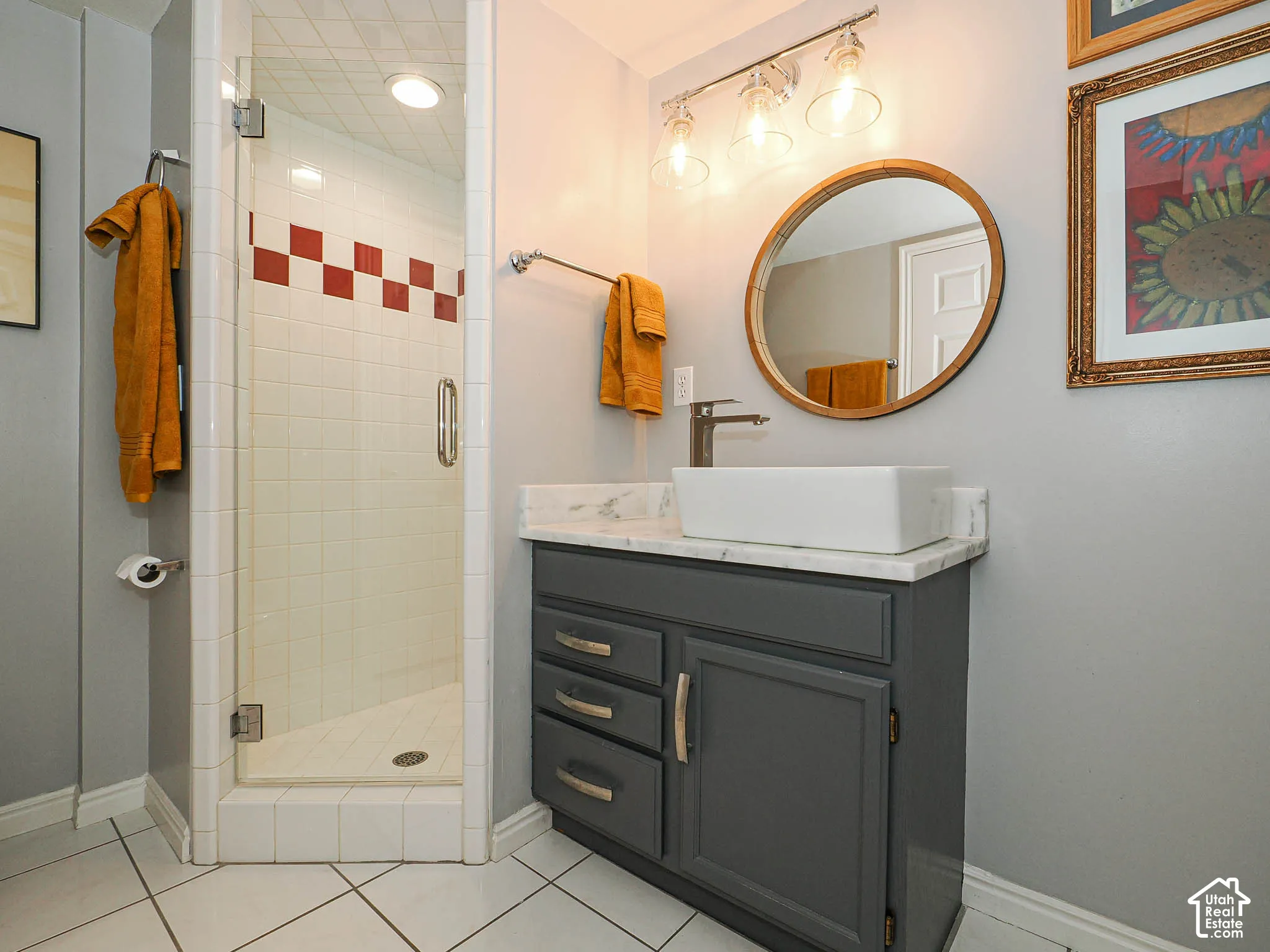 Glass-enclosed shower with tiled walls, contemporary vanity with a vessel sink, marble-finish countertop, and track lighting fixture