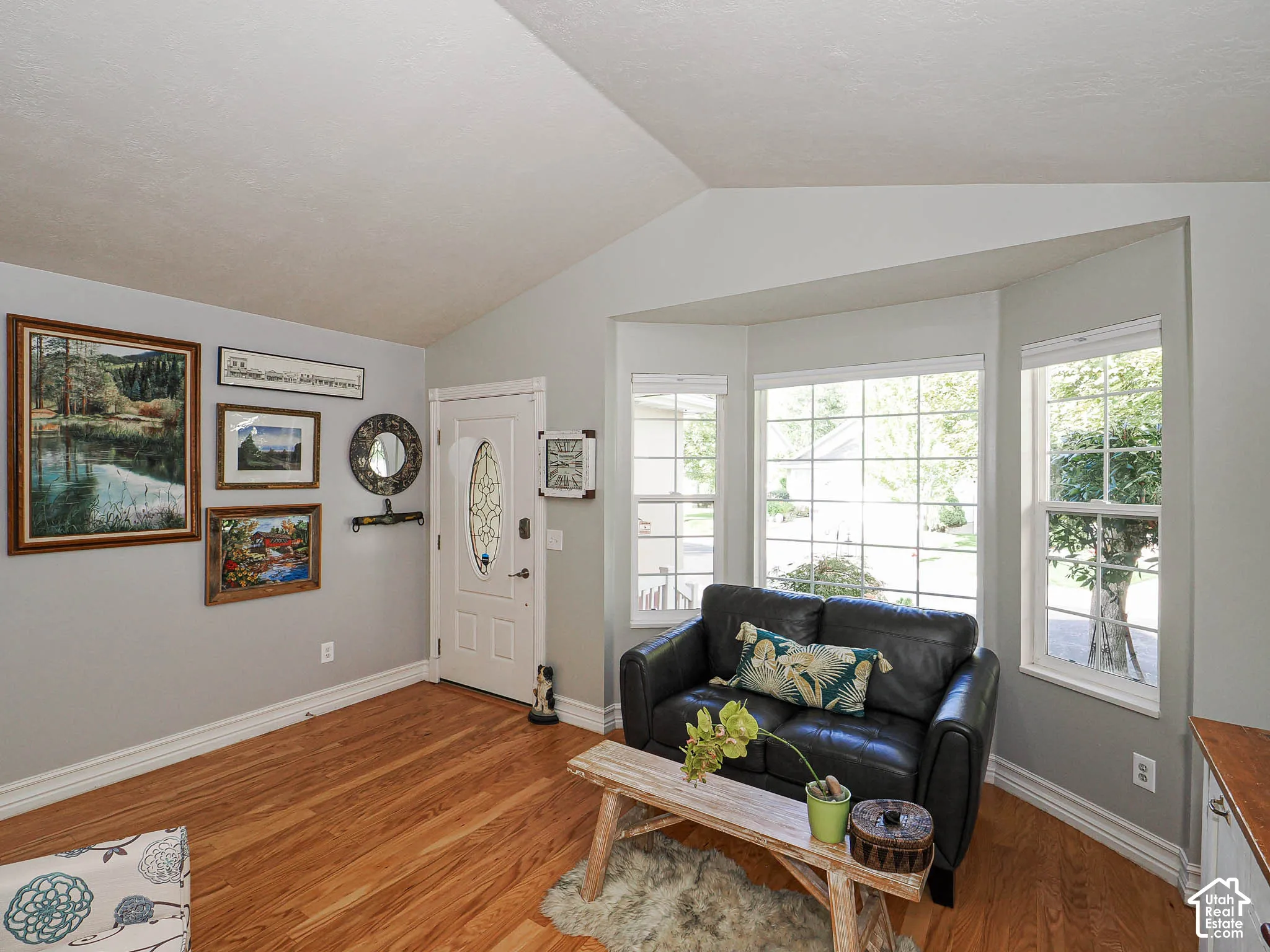 Vaulted ceiling with a bay window feature, wood-finish flooring, and white trim
