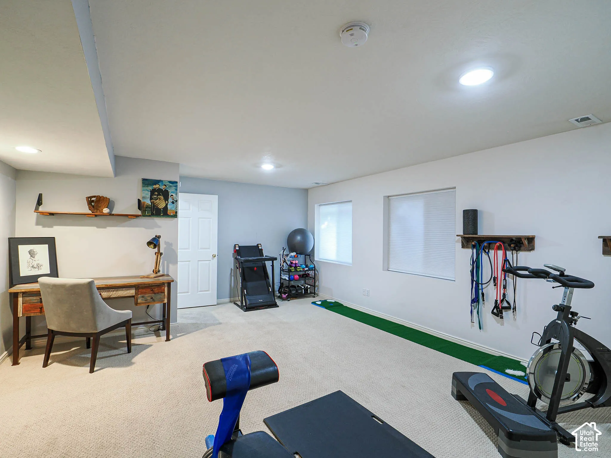 Recessed lighting illuminates this versatile space featuring light-toned carpeting and two windows with blinds