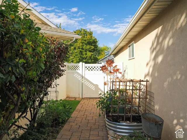 Brick paver pathway with a white lattice gate, stucco exterior, and raised garden bed