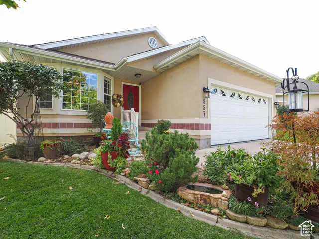 Stucco exterior featuring a bay window, red entry door, white garage door with decorative lites, and established landscaping